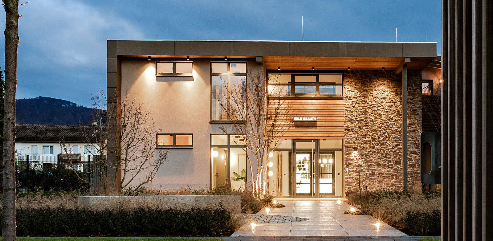 Wild Beauty Bürogebäude in modernem Stiel, mit Stein- und Holzfassade, beleuchtetet bei Dämmerung